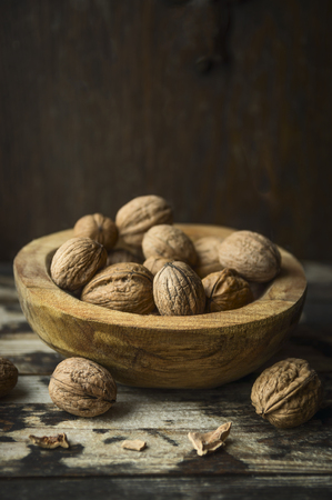 Walnuts with and without shell in a rustic bowl on kitchen table over wooden backgroundの写真素材