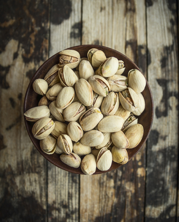 dish with salted pistachios in a wooden bowl on wooden rustic background, top viewの写真素材