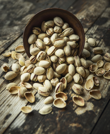 salted pistachios are scattered from a wooden bowl on wooden rustic background,top viewの写真素材