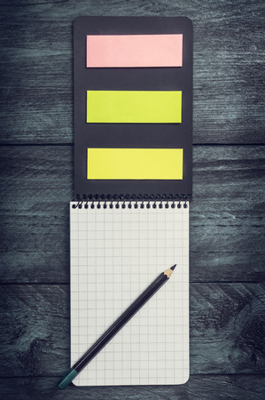 black notebook with a sheet in a cage with pencil and colored sticky notes on a wooden rustic background, top viewの写真素材