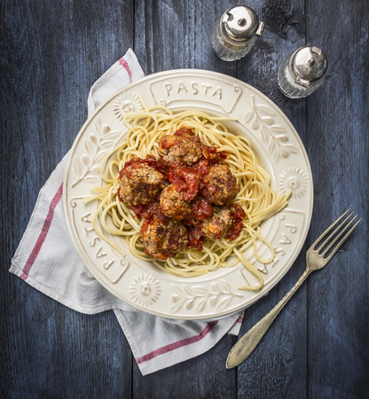 spaghetti with delicious meatballs made from ground beef in a spicy tomato sauce with salt pepper and fork in a plate with inscription pasta on wooden rustic background, top viewの写真素材