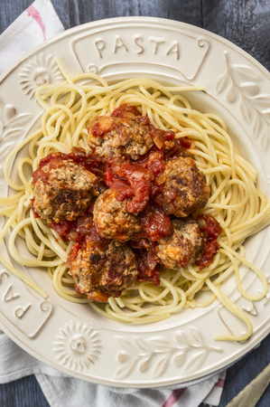 spaghetti with delicious meatballs made from ground beef in a spicy tomato sauce in a plate with inscription pasta on wooden rustic background, top viewの写真素材