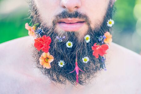 man's face with a beard with flowers in his beard close-up on green natural background, tonedの写真素材
