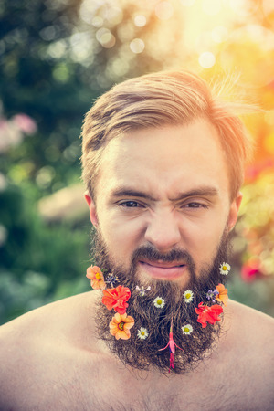 a man with an angry face with a beard with flowers in his beard On natural backgroundの写真素材