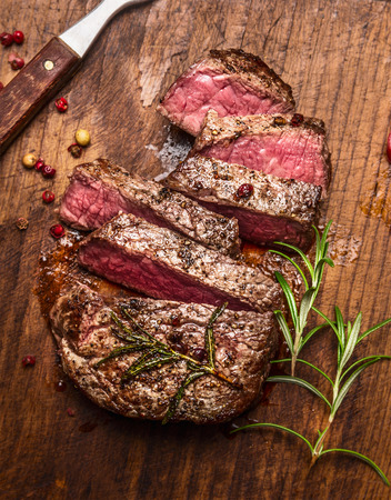 roasted ribeye steak sliced on a cutting board with a fork, rosemary and peppers, top view, close upの写真素材