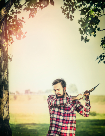 young bearded Lumberjack with Ax gut a tree on summer nature background.の写真素材