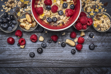 Red bowl with muesli, nuts and fresh berries on blue rustic background, to view, borderの写真素材