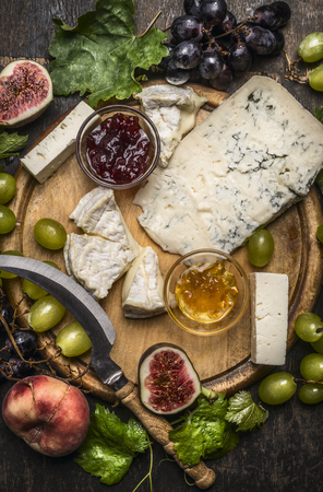 gorgonzola and Camembert cheese with Knife for cheese  white and dark grapes, honey and jam on a wooden cutting board on a dark rustic background top view close upの写真素材
