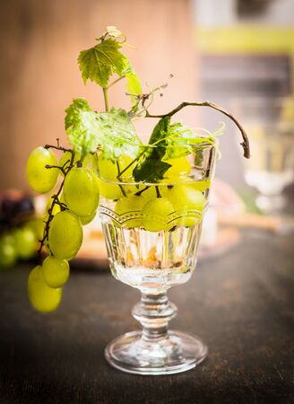 wine glass with a bright grapes on a branch and leaves on a dark wooden background close upの写真素材