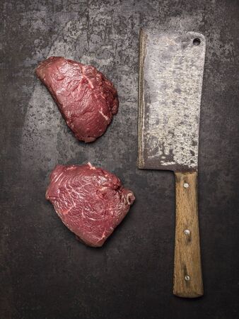 Two fresh raw beef steak with meat cleaver on dark rustic background top viewの写真素材