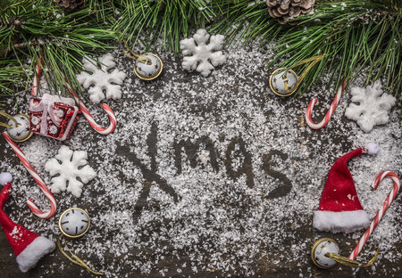 Christmas snowy background with the words x-mas Christmas candy, hat and  pine branches and pine cone on  wooden rustic background top viewの写真素材