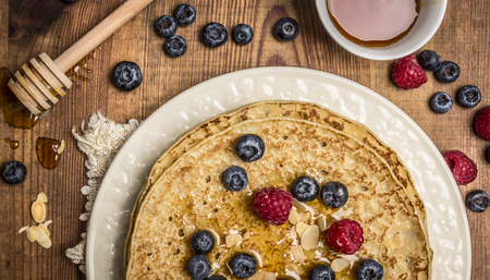 delicious pancakes with fresh berries with honey, almonds cup of tea with honey spoon on white plate with napkin on wooden rustic background top viewの写真素材