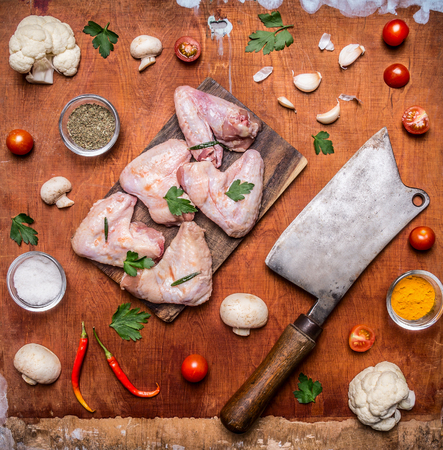 raw chicken wings with parsley on a cutting board Meat cleaver sharp red pepper cauliflower mushrooms seasoning tomatoes on rustic wooden background top viewの写真素材
