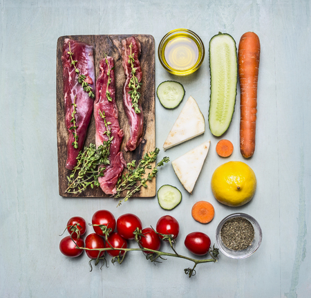 fresh slices of raw lamb with herbs, spices, oil and lemon and vegetables on the cutting board lined rectangle on wooden rustic background top view close upの写真素材