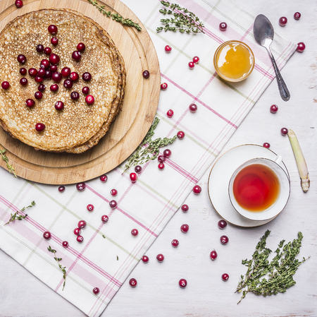 pancakes with honey and cranberries, a cup of tea with thyme and a spoon on a cutting board on a napkin on wooden rustic background top viewの写真素材