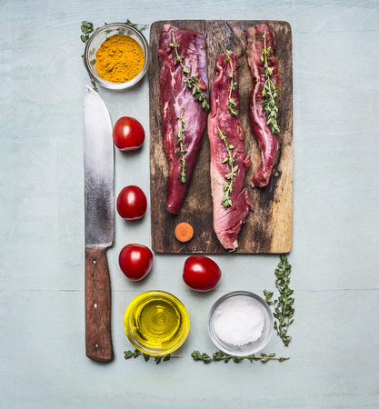 fresh pieces of raw lamb on a chopping board, with herbs, spices, cherry tomatoes, lined rectangle on wooden rustic background top view close upの写真素材