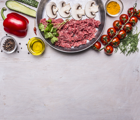 raw minced meat with mushrooms in a pan, pepper, tomatoes on a branch, spices, cucumbers  border ,with text area, on wooden rustic background top viewの写真素材