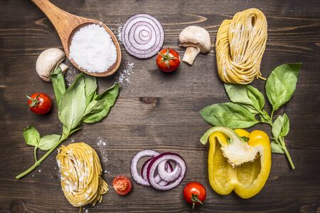 Ingredients for cooking raw pasta with mushrooms, peppers, basil and onions on wooden rustic background top view close up border, place for textの写真素材