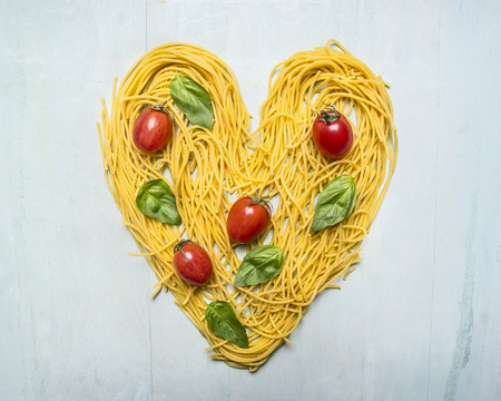 raw pasta with cherry tomatoes and basil leaves lined heart, valentines day on wooden rustic background top view close upの写真素材