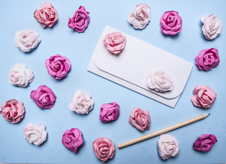 white envelope on a blue background with colorful paper roses border, place for text decorations for Valentine's Day top view close upの写真素材