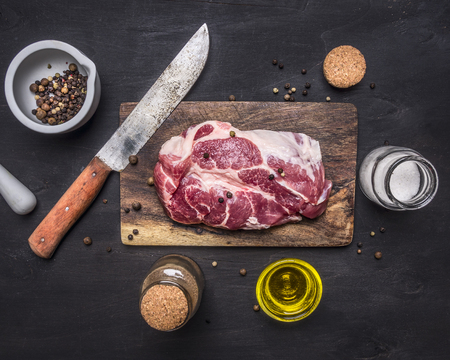 raw pork steak with herbs, oil knife for meat on a cutting board on wooden rustic background top view close upの写真素材