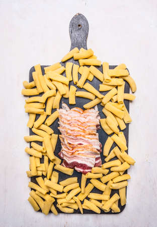 raw penne pasta and delicious ham on a cutting board, lined frame on wooden rustic background top view close upの写真素材