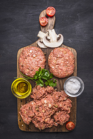 two cutlets for burgers with minced meat, herbs, butter and salt  on wooden rustic background top view close upの写真素材