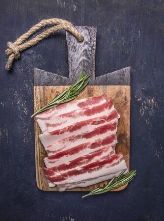 delicious raw bacon with rosemary on vintage cutting board on wooden rustic background top view close upの写真素材
