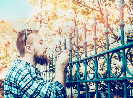 man in a plaid shirt with a beard and sunglasses smelling the spring flowers of cherryの写真素材