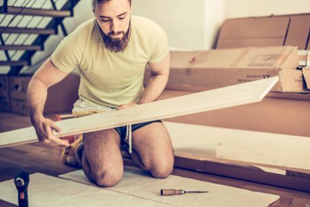 young man collect furniture in the new apartment, holding and looking at the detail of sitting on the floorの写真素材