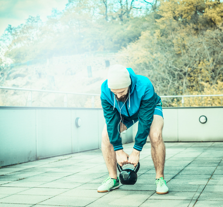 Training on the terrace of the house, overlooking the forest, the young man with a beard lifts weightsの写真素材