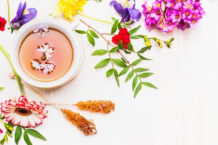 different multicolored flowers lined up around a cup of tea, sugar sticks, top viewの写真素材