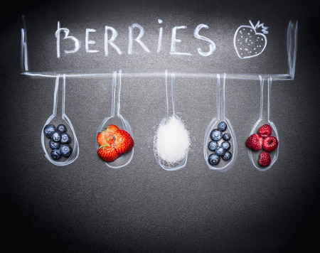 Various berries for jam and sugar, are in painted spoons on chalkboard top viewの写真素材