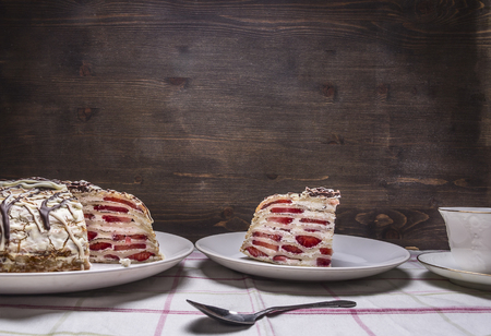 piece home strawberry cake with icing, with a cup of tea and a spoon on the tablecloth place for textの写真素材