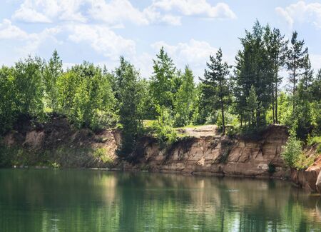 coast forest lake with crystal clear water, which reflects the trees, beautiful prorodny landscape with blue skyの写真素材