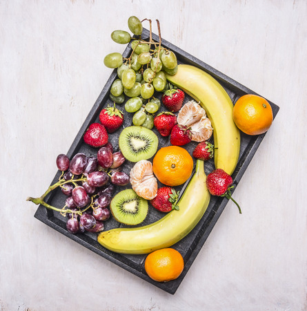 Detox and diet food concept,  fresh fruit, bananas, grapes, kiwi and tangerine, strawberry lined in vintage wooden box top viewの写真素材