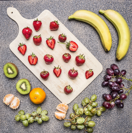 Superfoods and healthy lifestyle or detox diet food concept bananas, strawberries, light and dark grapes, kiwi and tangerine on a granite table top viewの写真素材