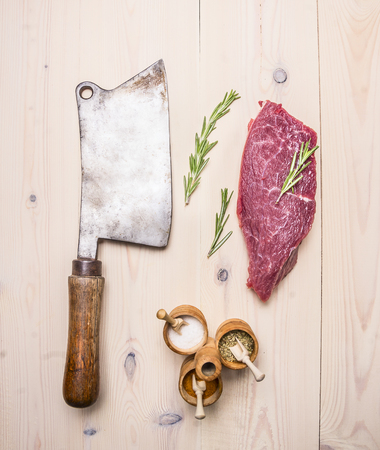 large meat cleaver, with beef steak, rosemary and various spices on wooden rustic background top view close upの写真素材