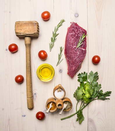 concept cooking raw beef steak, rosemary, wooden hammer for beating the meat, oil, herbs and spices on wooden rustic background top view close upの写真素材