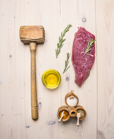 concept cooking raw beef steak, rosemary, wooden hammer for beating the meat, oil, herbs and spices on wooden rustic background top view close upの写真素材