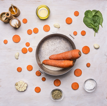 Healthy foods, cooking and vegetarian concept. sliced carrots with spinach and spices, laid out around a vintage pots cooking vegetable soup on wooden rustic background top view close upの写真素材
