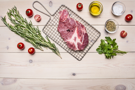 raw pork steak on the grill for cooking with rosemary, cherry tomatoes and spices, whole pepper border ,place for text  on wooden rustic background top view close upの写真素材
