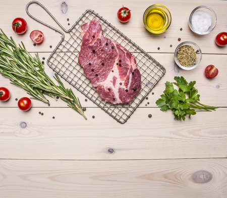 raw pork steak on the grill for cooking with rosemary, cherry tomatoes and spices, whole pepper border ,place for text  on wooden rustic background top view close upの写真素材