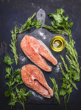 two raw steak to salmon, seafood, healthy food with herbs, parsley, olive oil and salt on dark vintage cutting board on wooden rustic background top view close upの写真素材