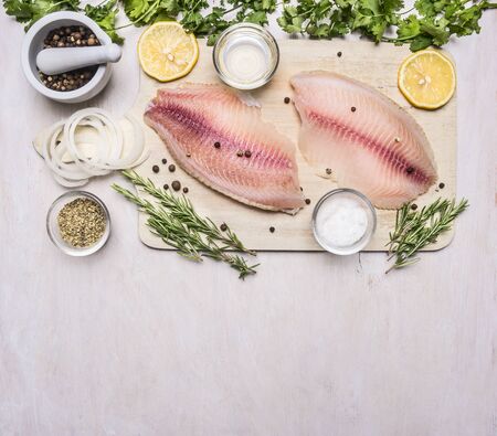 raw fillet of tilapia with spices and herbs, lemon and pepper on a cutting board on a white background rustic village top viewの写真素材