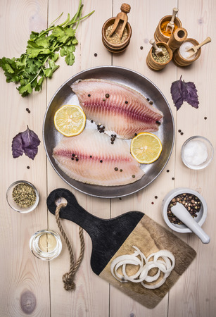 concept cooking tilapia fillets with lemon on a vintage pan with herbs, vegetables and spices on wooden rustic background top view close upの写真素材