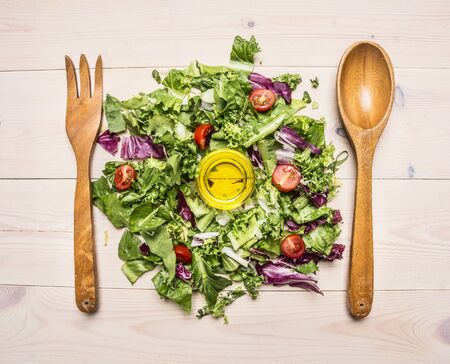 fresh salad mix, cooking vegetarian salad, lie next to a wooden spoon and fork to mix the salad on wooden rustic background top view close upの写真素材