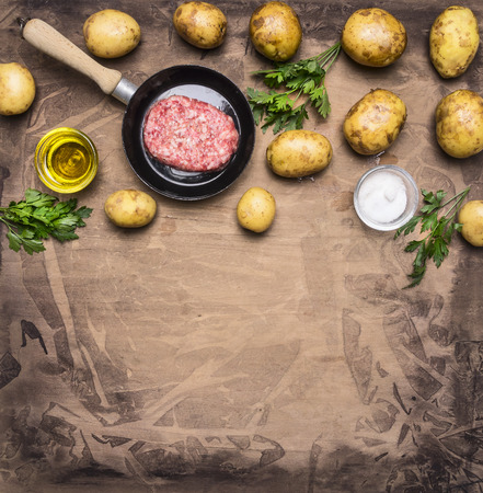 cooking homemade hamburger with fried potatoes, fresh ground beef in a small frying pan with herbs, oil and spices on wooden rustic background top view close up border place for textの写真素材