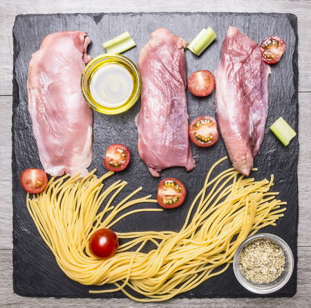 raw duck breast with spaghetti, cherry tomatoes, black pepper, chopped onions and other seasonings, laid out on the marble rustic cutting board, top viewの写真素材