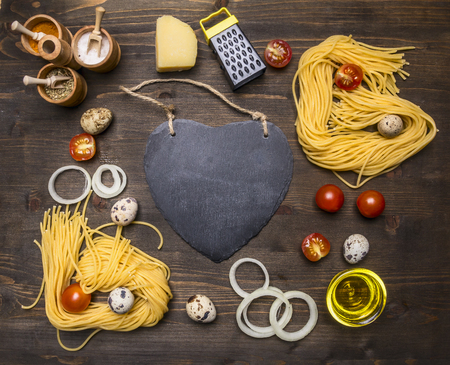 ingredients for cooking vegetarian pasta cherry tomatoes, onions, parmesan cheese, a variety spices rustic wooden background, lined frame around cutting board in the form of heart with space for textの写真素材